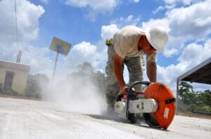 Man cutting concrete roadway against a blue sky with clouds