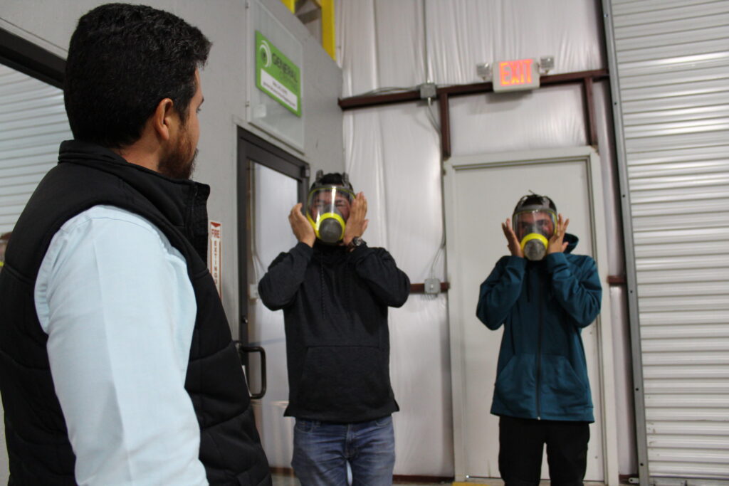 Two men demonstrating the property way to wear a respirator as a safety instructor looks on