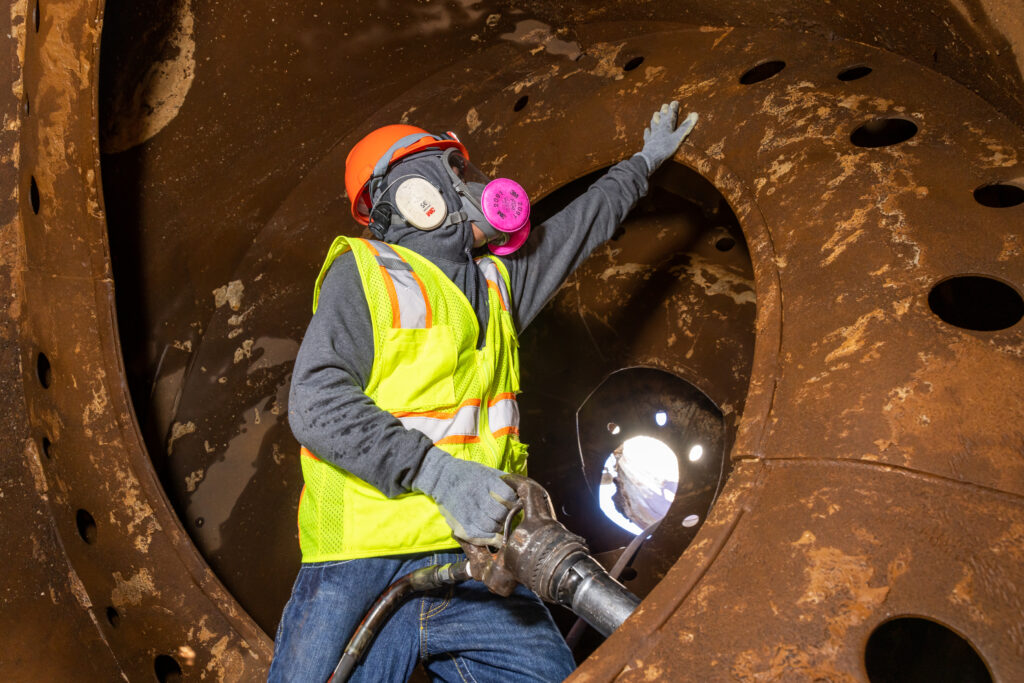 a man wearing safety gear holding a hand jackhammer inside a concrete drum