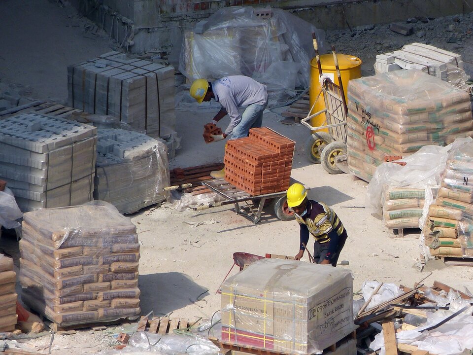 Concrete workers in PPE surrounded by bricks, bagged cement and building materials