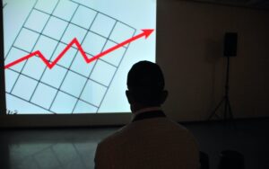 Man in dark room looking at projection of red arrow on graph