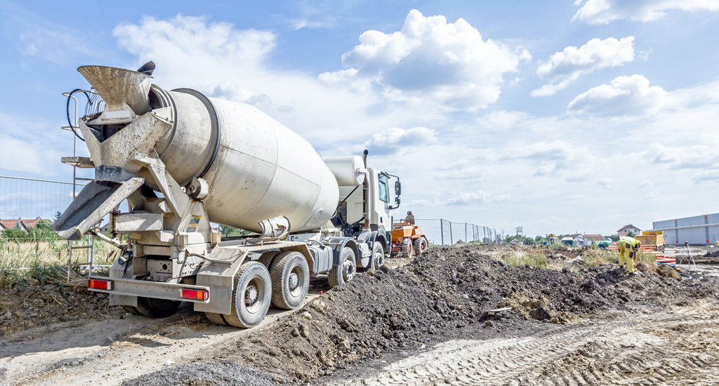 Redi mix concrete truck and construction worker on a job site against a blue sky with clouds