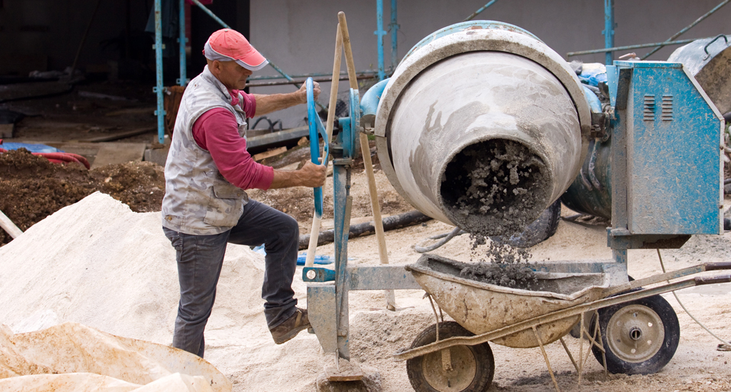 Man pouring material from a concrete mixer into a wheelbarrow on a job site