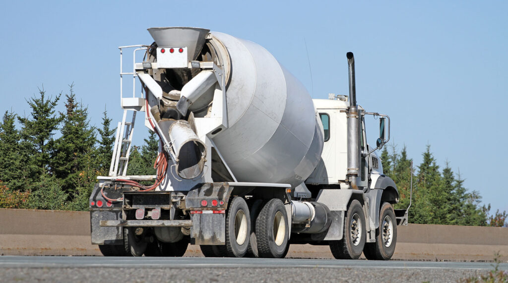 White ready mix concrete truck on a highway surrounded by evergreen trees