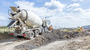 Ready mix concrete truck traveling over dirt against blue sky with clouds