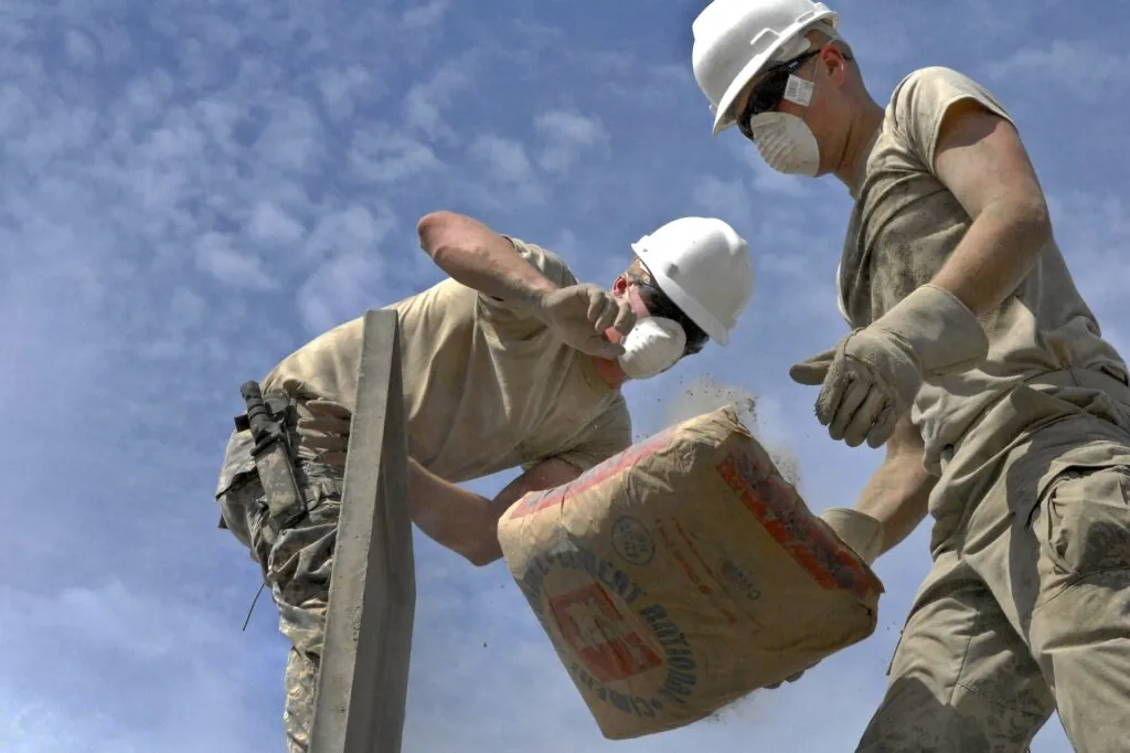 Men in hard hats and face masks moving bagged cement