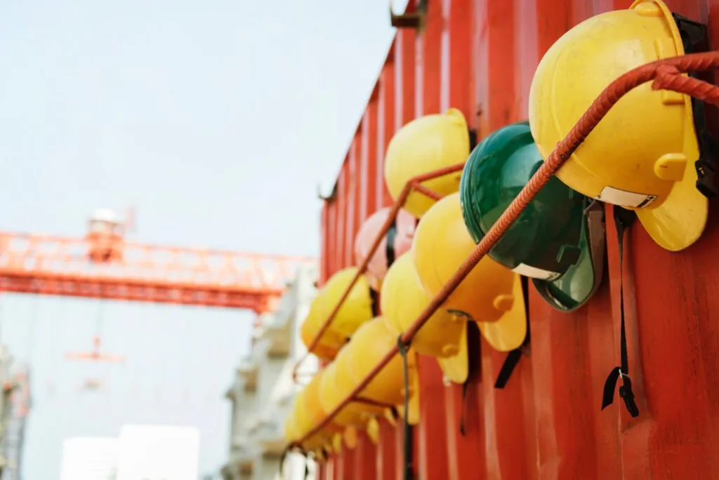 Yellow and green hard hats resting on a rebar shelf attached to an orange steel building